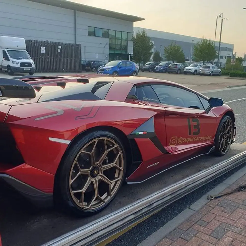 A red Lamborghini Aventador on the deck of an ICM transporter, loaded at the kerbside
