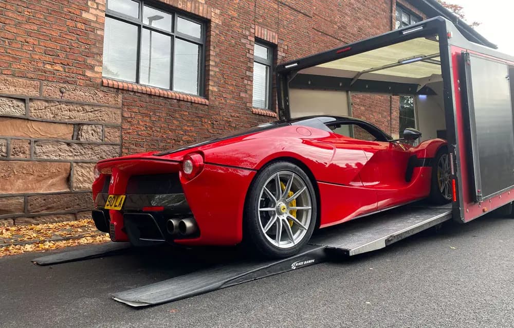 A red Ferrari 488 part-way up an ICM transporter ramp beside a building