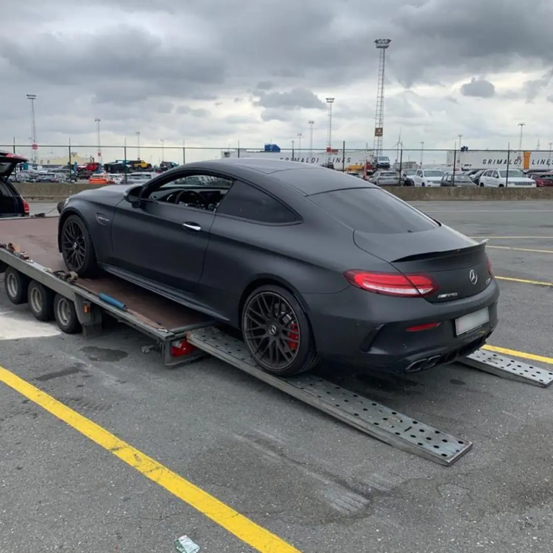 A grey Mercedes coupé on an ICM trailer at a port compound
