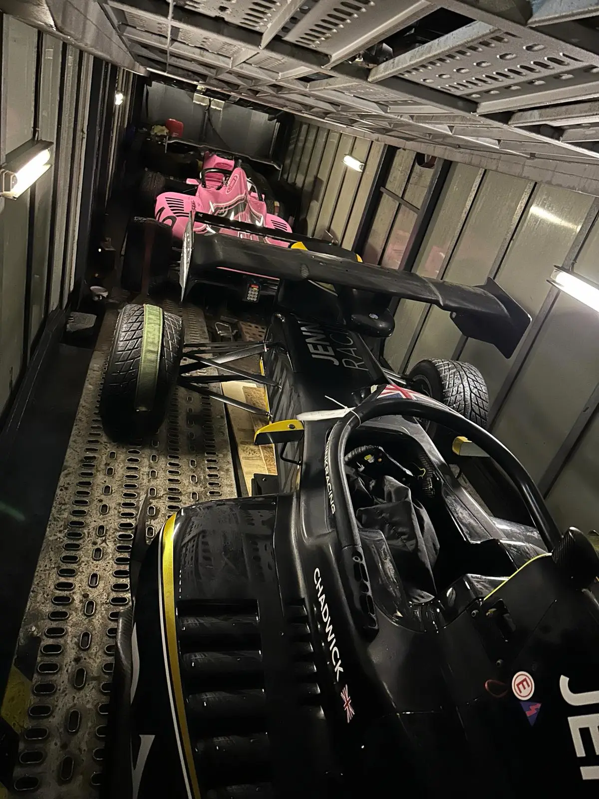 A single-seat racing car strapped down on the upper deck of an ICM enclosed transporter, with a second car below