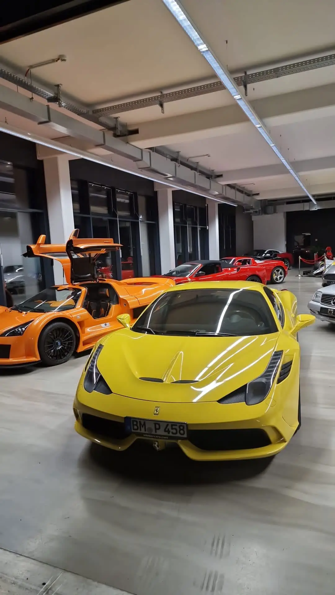 A line of supercars in a showroom, including a yellow car in the foreground